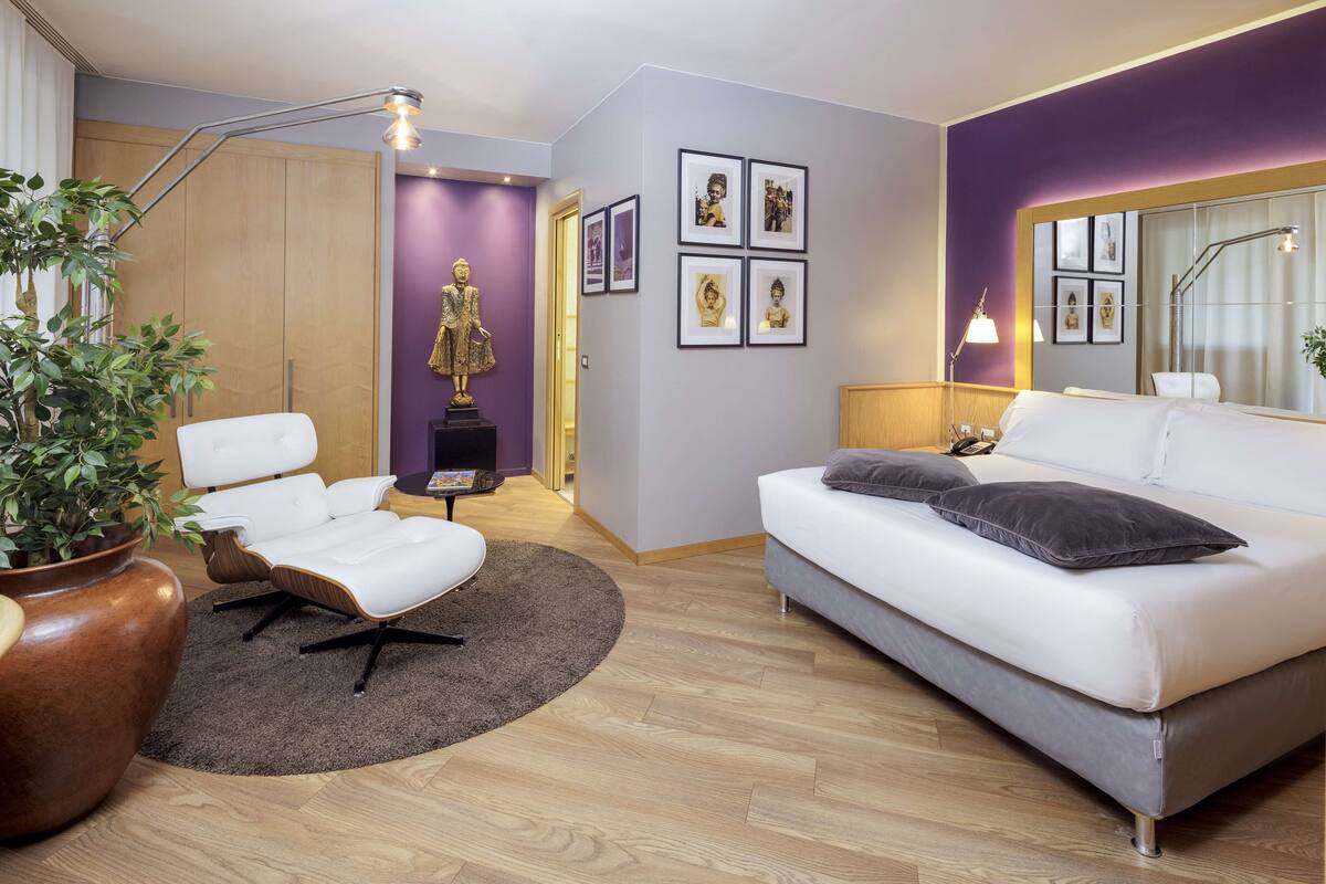 A modern living room with a white sofa, a white armchair, a large potted plant, and a wooden wardrobe.