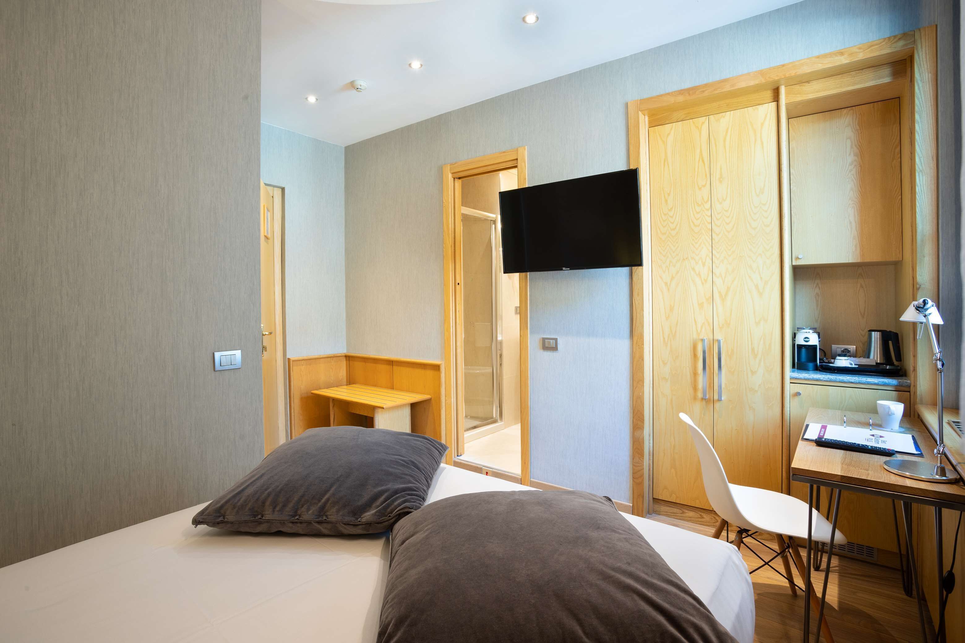 A hotel room with a bed, a desk, a chair, a TV, and a wardrobe.