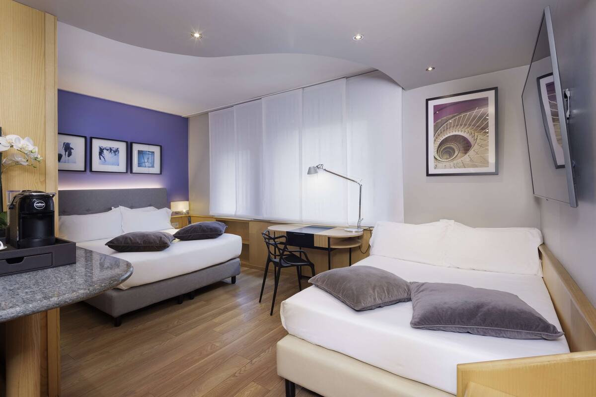 A modern hotel room with two beds, a desk, and a chair.