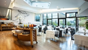 A modern dining area with a high ceiling, large windows, and a central serving station.