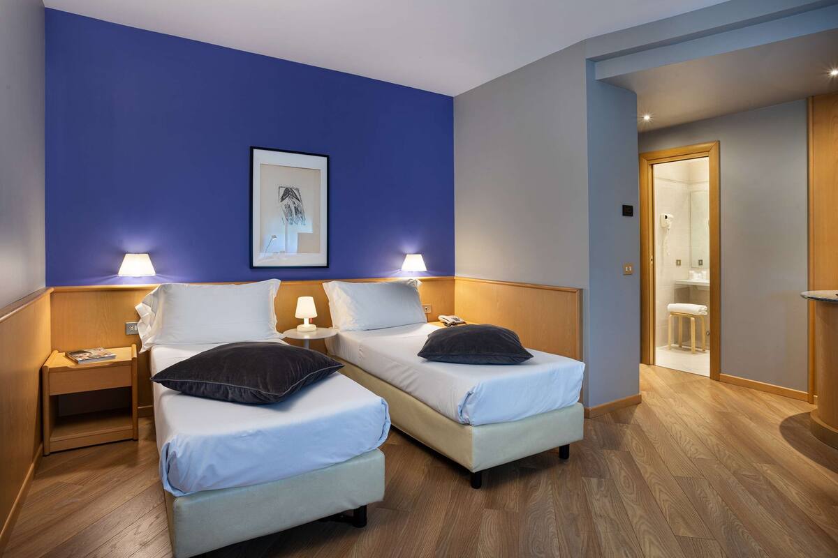 A hotel room with two beds, a framed picture on the wall, and a bathroom visible through an open door.