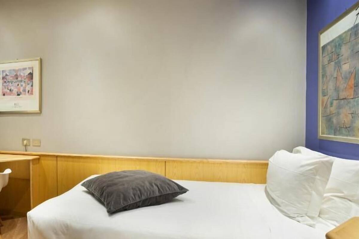 A hotel room with a bed, a desk, a chair, a television, and a framed picture on the wall.
