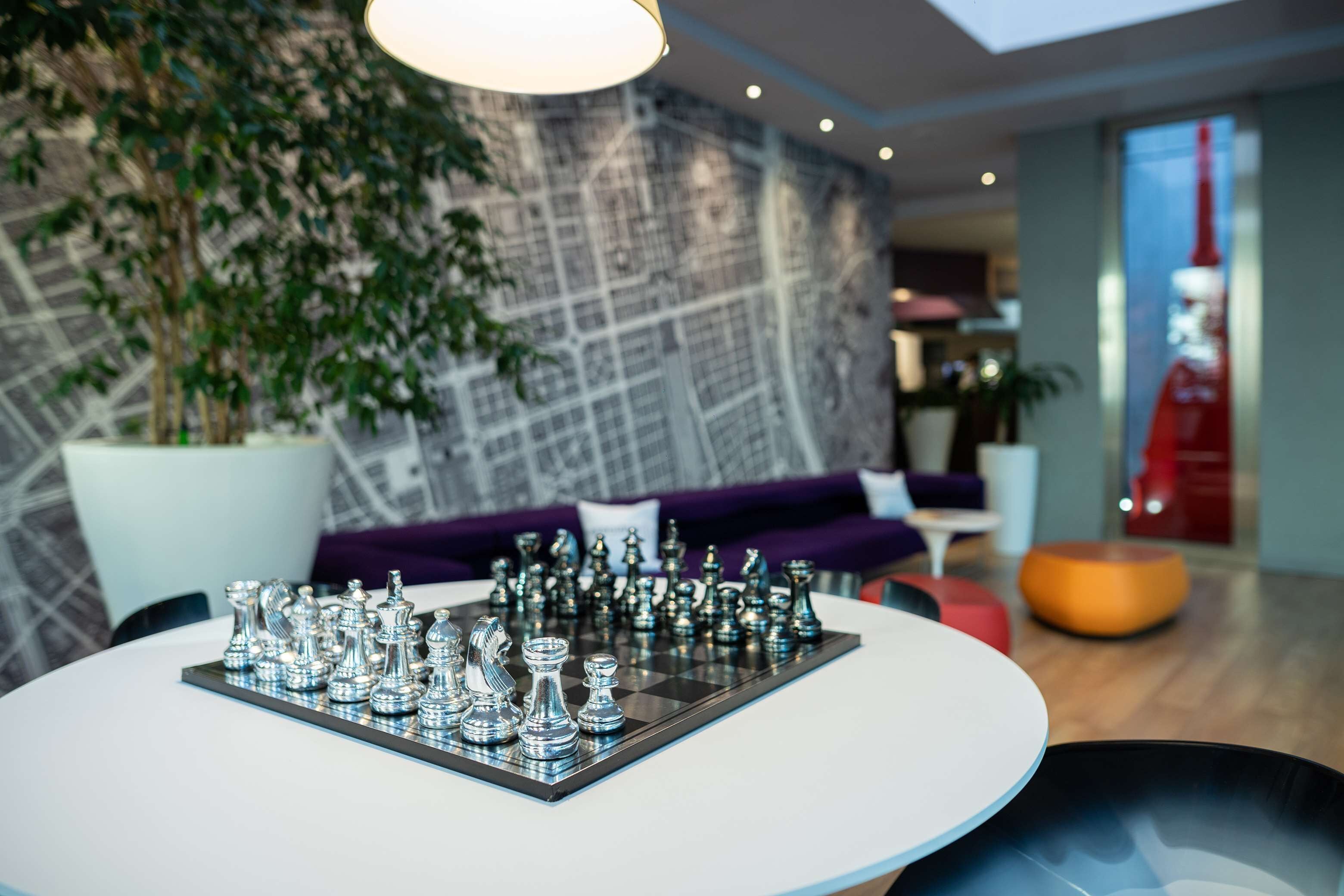 A modern interior with a chessboard on a white table, a large potted plant, and a purple sofa in the background.