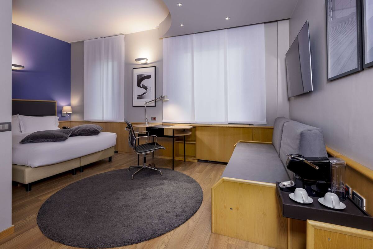 A modern hotel room with a bed, desk, and seating area.