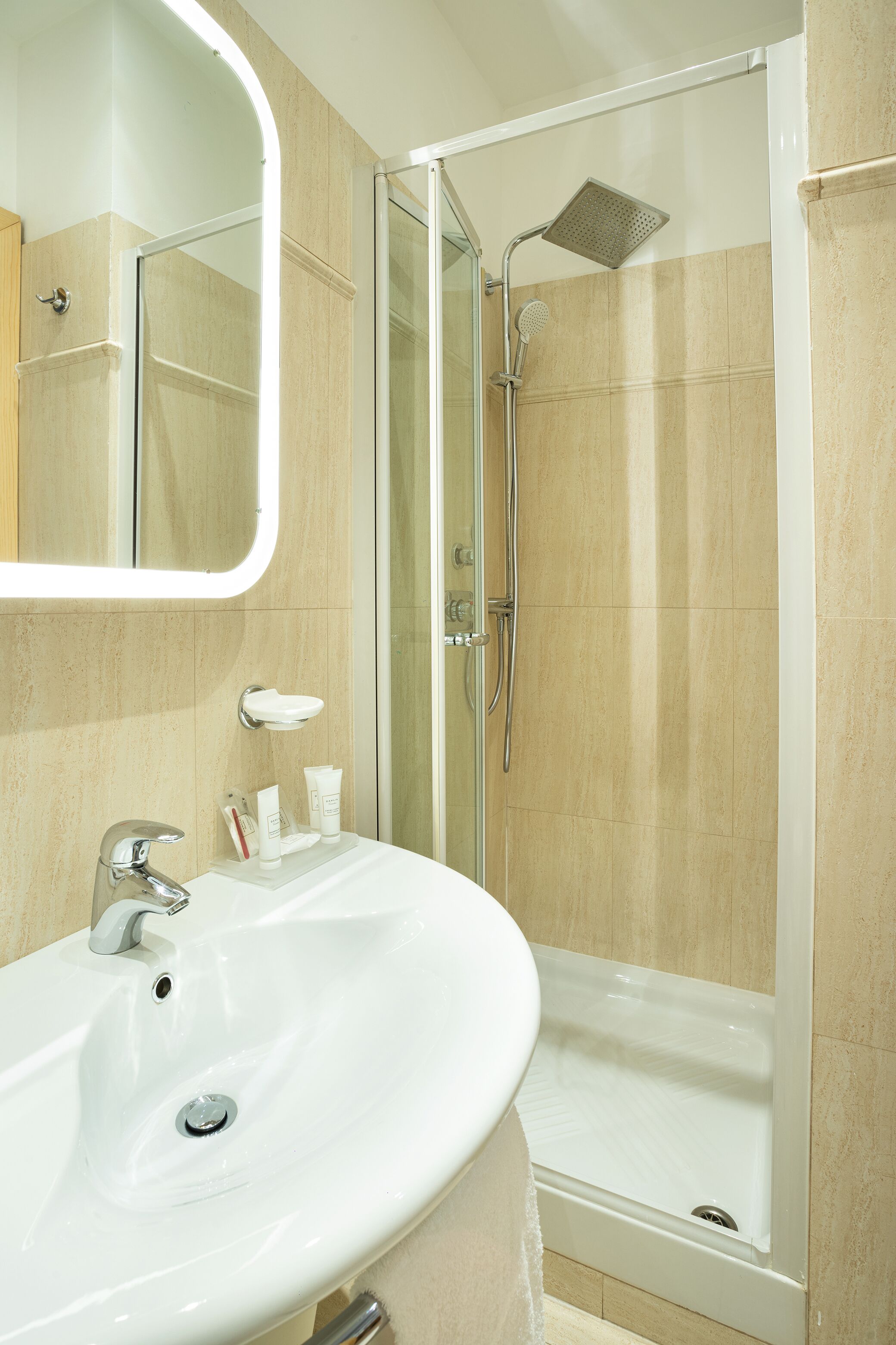 A bathroom with a white sink, a mirror, a shower with a glass door, and beige tiles.