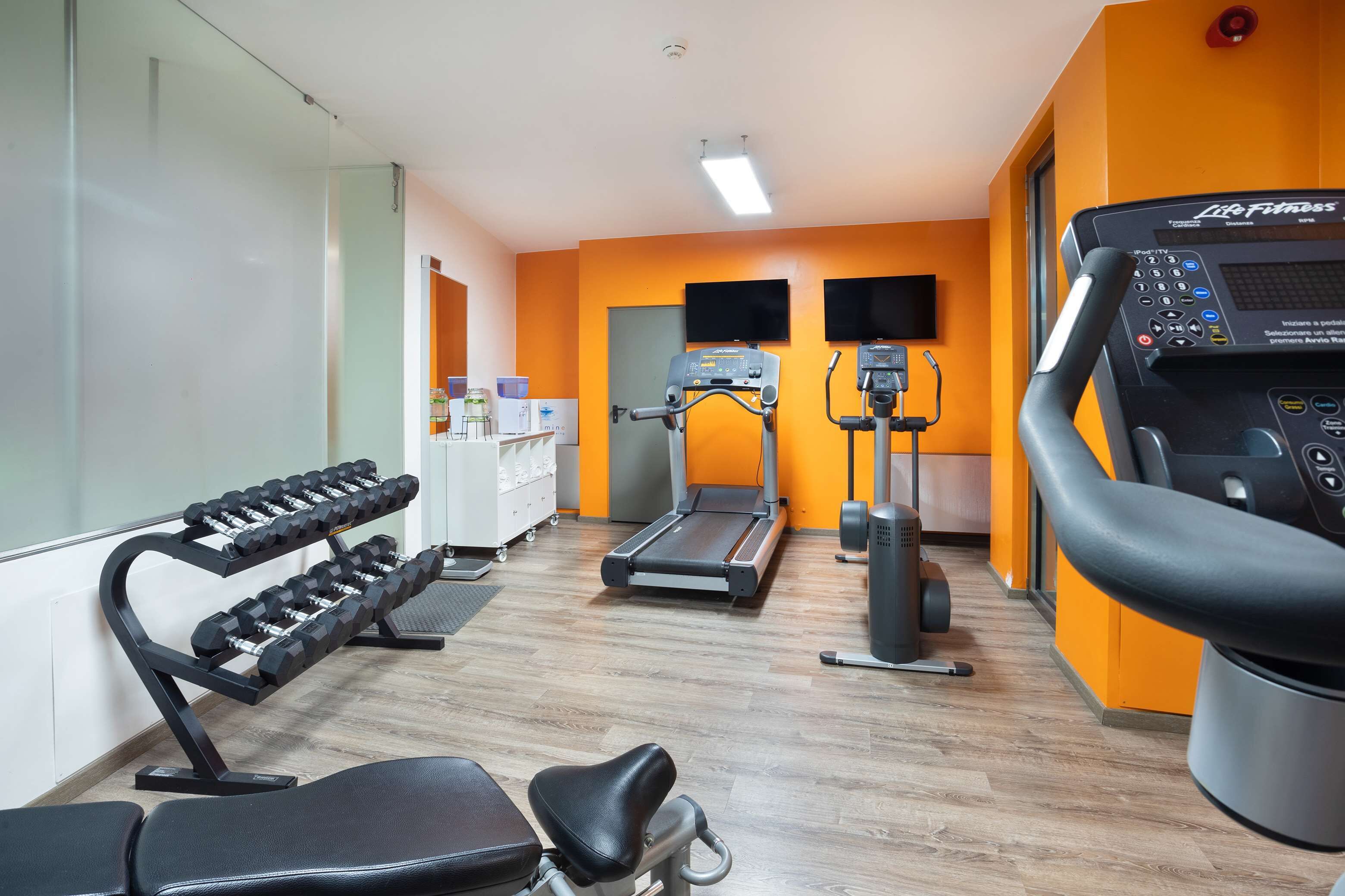 Een sportschool met trainingsapparatuur, waaronder gewichten, loopbanden en een hometrainer.