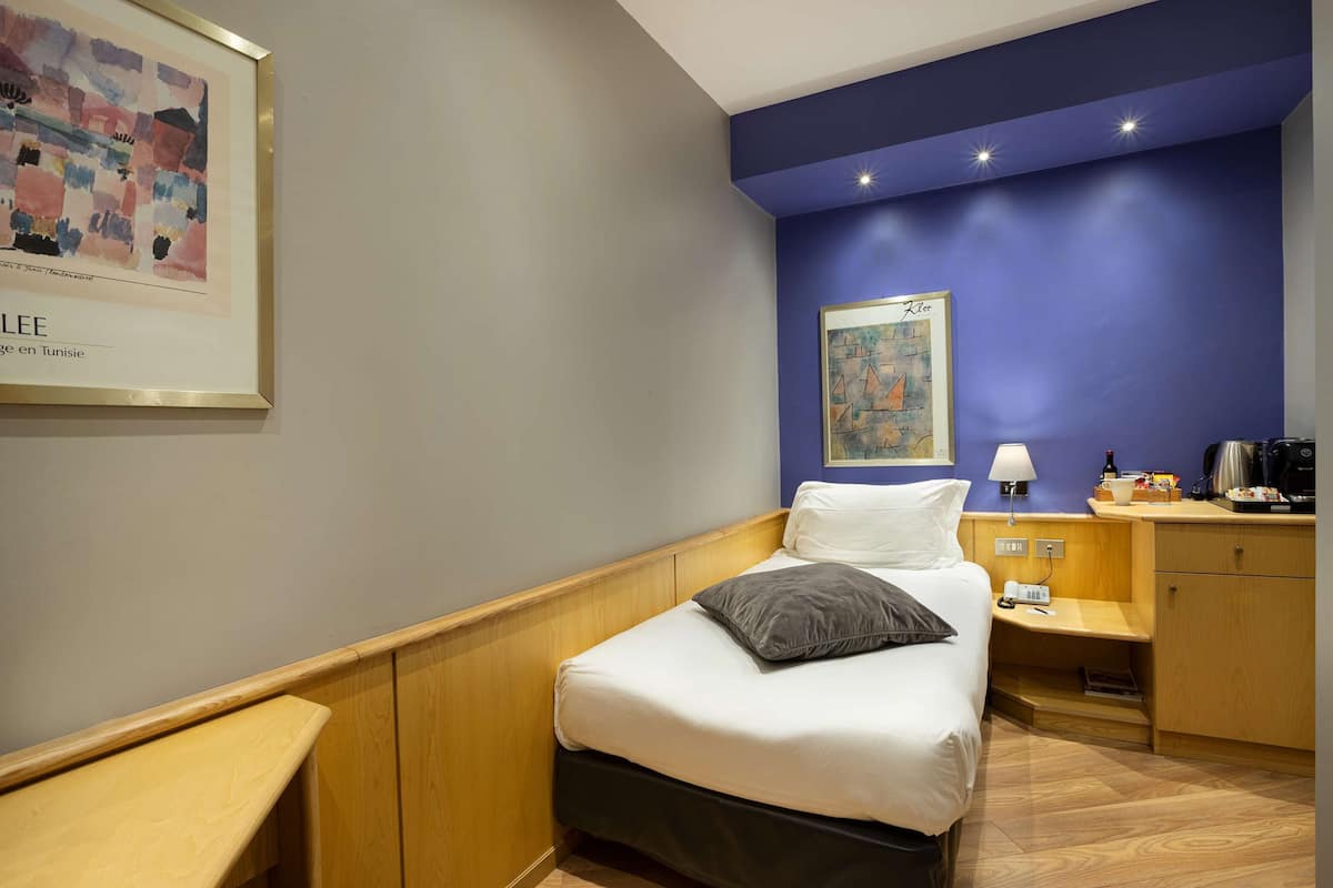 A neatly arranged hotel room with a bed, a nightstand, a desk, and a wall-mounted lamp.