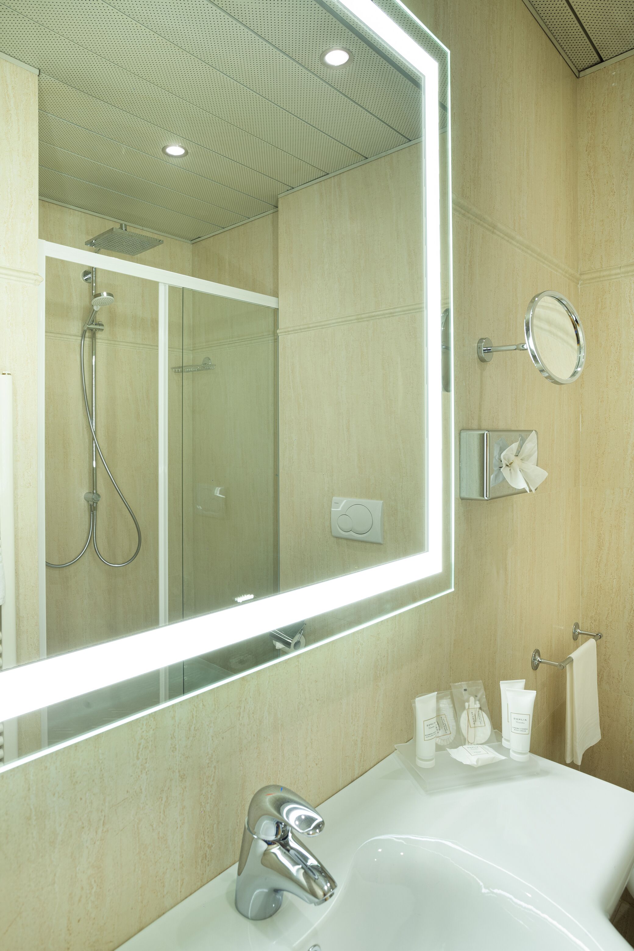 A modern bathroom with a large mirror, a shower, a sink, and toiletries.