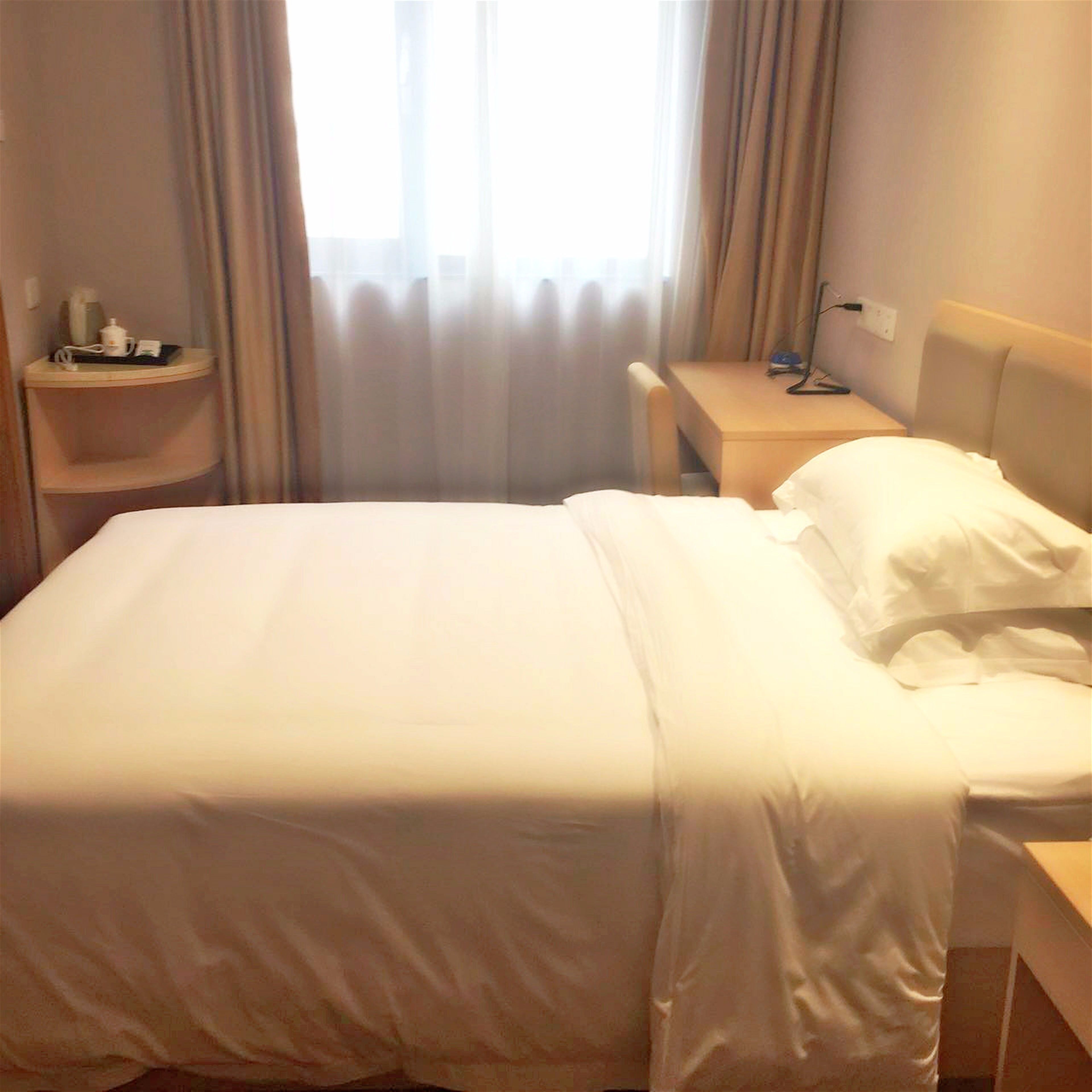A hotel room with a bed, a bedside table, and a chair.