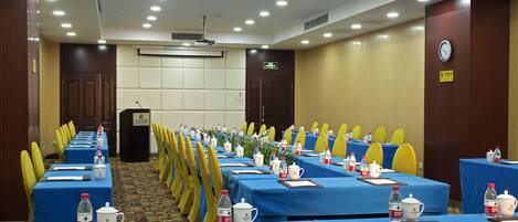 A conference room with rows of tables, chairs, and various amenities like water bottles, cups, and notepads.