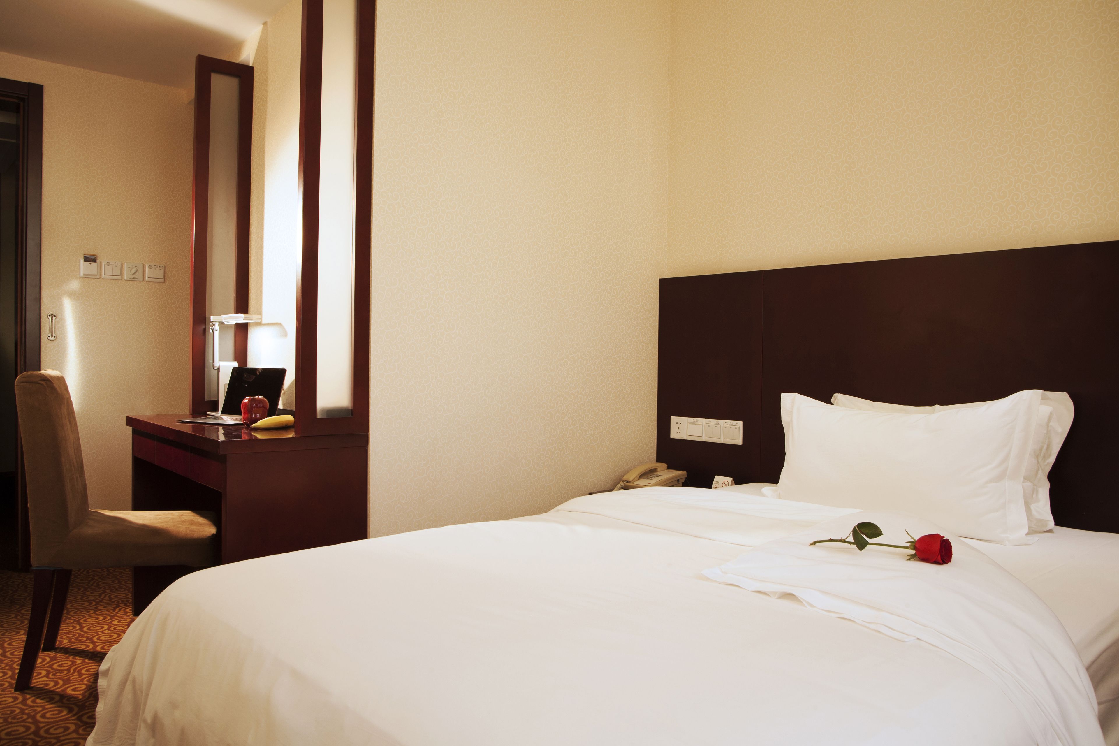 A hotel room with a bed, a desk with a telephone, a chair, and a mirror.