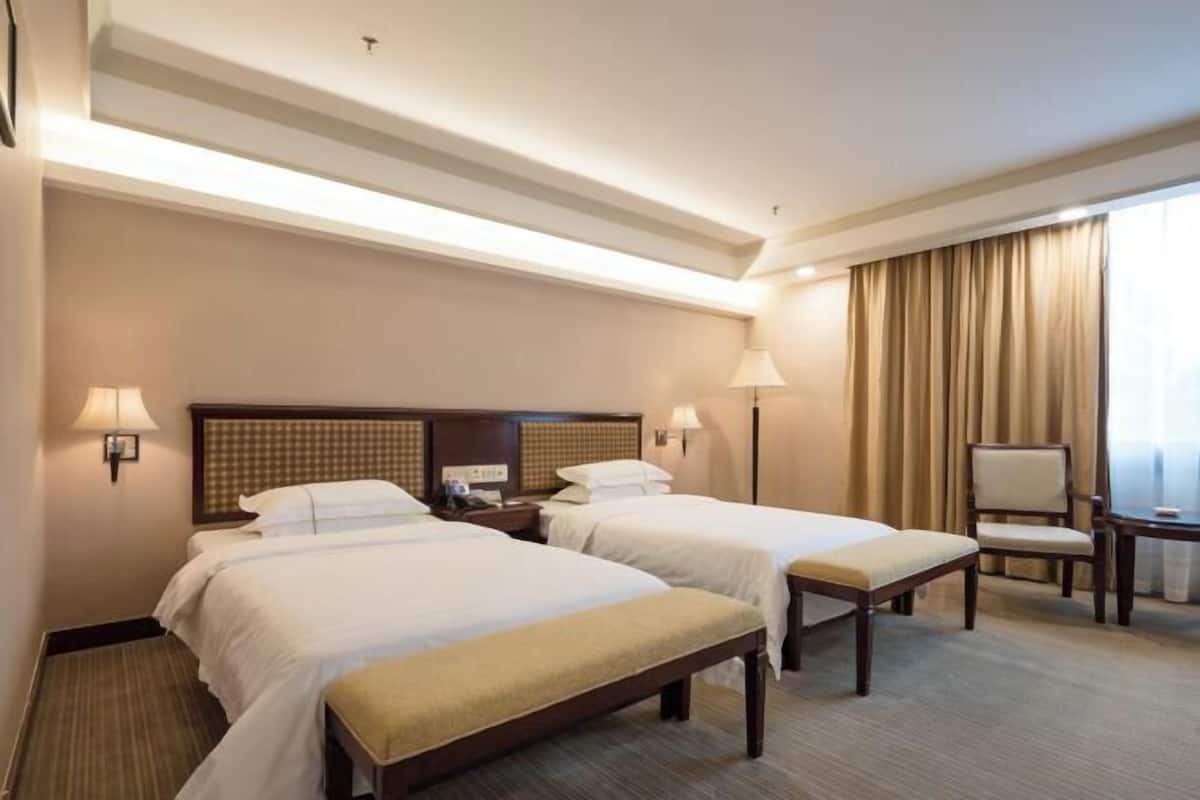 A hotel room with two beds, a desk, a chair, and a window with curtains.