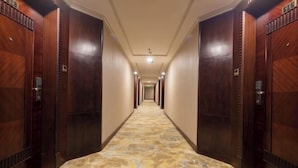 A hotel corridor with wooden doors, a patterned carpet, and a ceiling light. - Zhong Hua Hotel (Guangzhou)