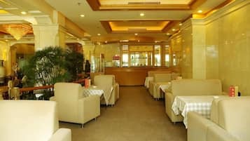 A hotel dining area with multiple tables and chairs, a central bar, and a large plant.