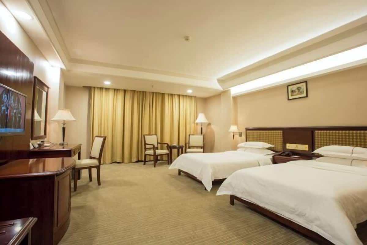 A hotel room with two beds, a desk, chairs, and a television.