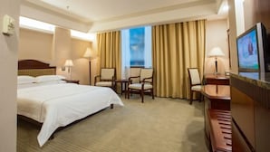 A hotel room with a large bed, two chairs, a desk, a television, and a window with curtains. - Zhong Hua Hotel (Guangzhou)
