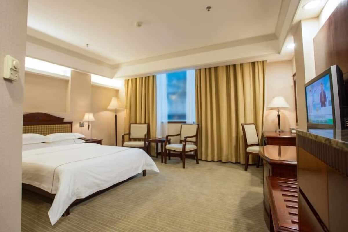 A hotel room with a large bed, two chairs, a desk, a television, and a window with curtains.