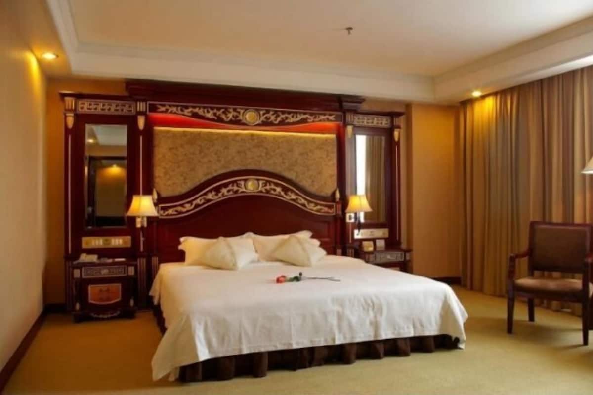A hotel room with a large bed, two bedside tables, a chair, and a mirror.