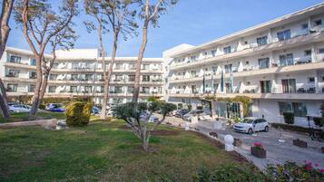 A multi-story hotel with balconies, a parking area, and a well-maintained lawn with trees.