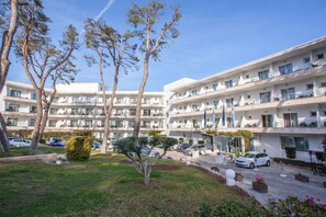 Un hotel de varios pisos con balcones, un estacionamiento y un césped cuidado con árboles.