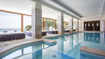 Ein moderner, überdachter Pool mit klarem, blauem Wasser, Steinpfeilern und Blick auf das Meer.