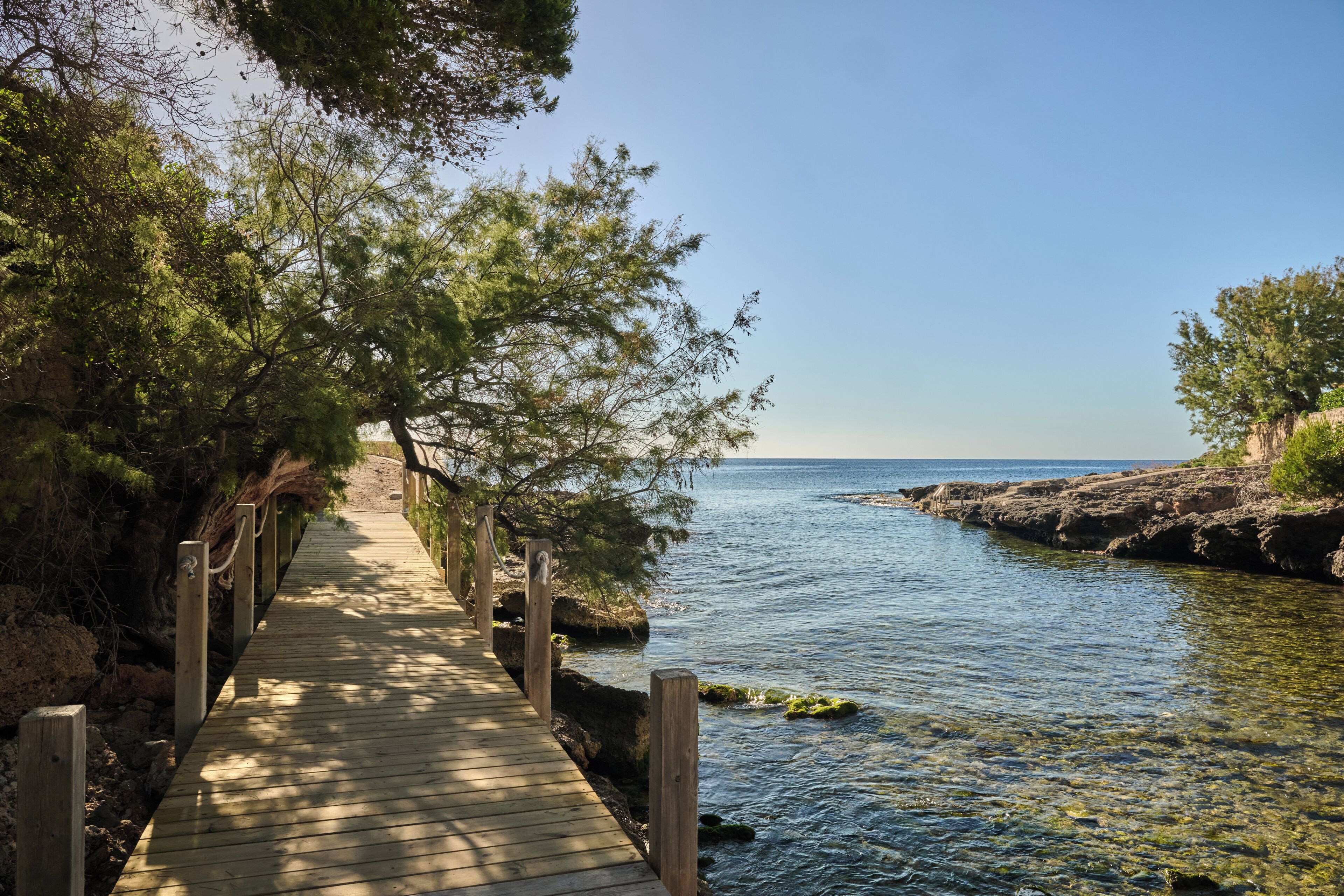 Passerella de fusta que condueix a una riba rocosa amb aigua cristal·lina.