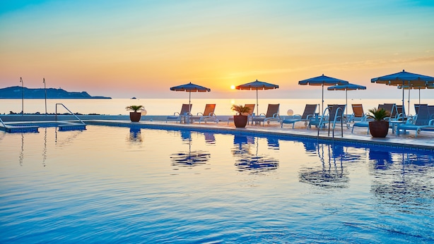 A poolside area with lounge chairs and umbrellas, a clear sky, and a sunset. - Grupotel Aguait Resort & Spa - Adults Only (Capdepera)