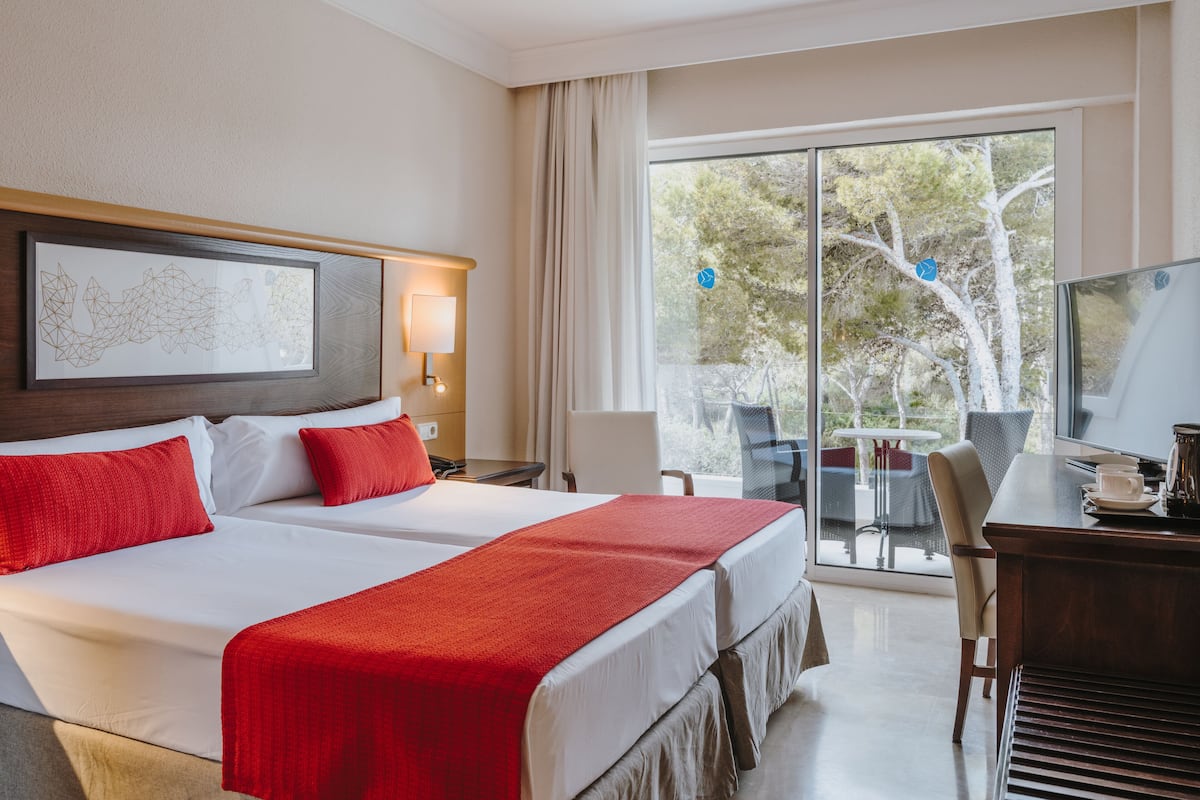 A hotel room with a large bed, a desk, and a view of trees through the window.