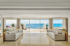 Amplia habitación con un gran ventanal corredero que da a una terraza exterior con vistas al mar. Hay dos sofás y una mesita en la habitación.