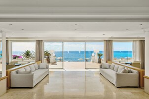 A spacious room with a large sliding glass door leading to an outdoor terrace with a view of the sea. There are two sofas and a small table in the room.