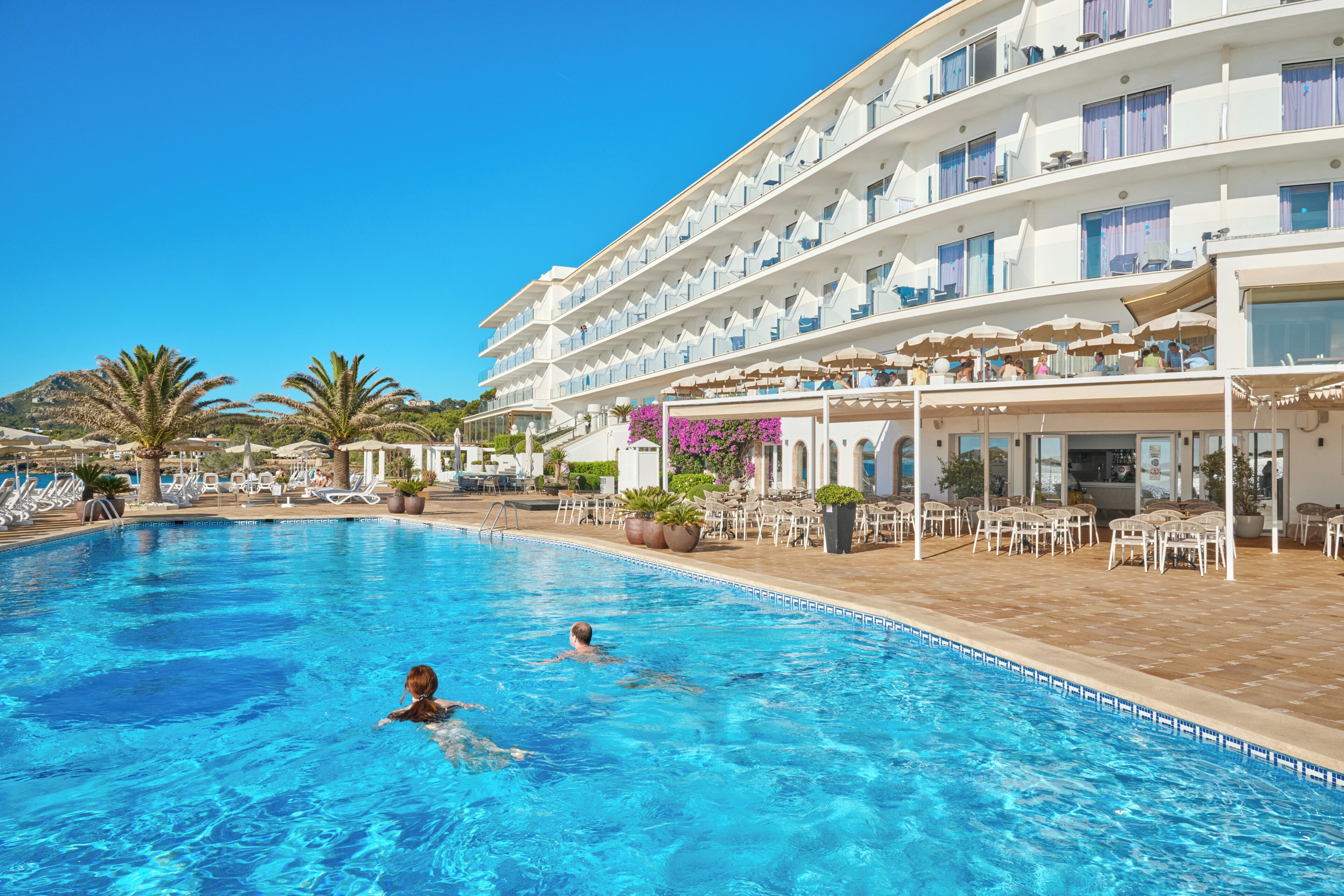 Een hotel met zwembad, terras en uitzicht op de bergen.