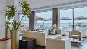 A modern hotel room with a large window overlooking the sea, a sofa set, a coffee table, and potted plants. - Grupotel Aguait Resort & Spa - Adults Only (Capdepera)