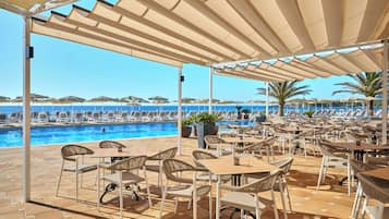 Ein Poolbereich mit Liegestühlen und Tischen, freier Blick auf das Meer und eine überdachte Sitzgelegenheit mit Sonnenschirmen.