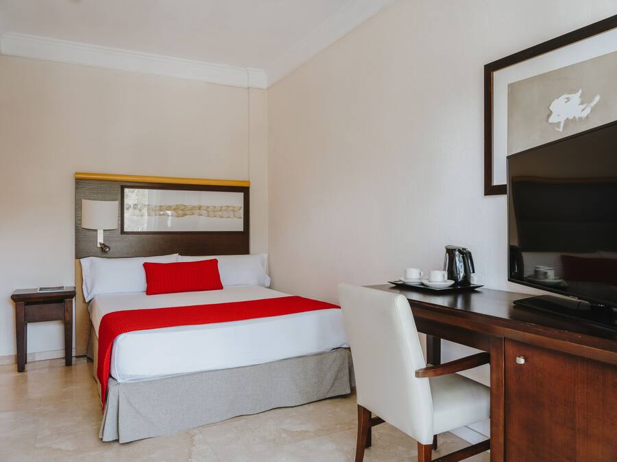 Una habitación de hotel con cama, escritorio, silla, televisor y cafetera.