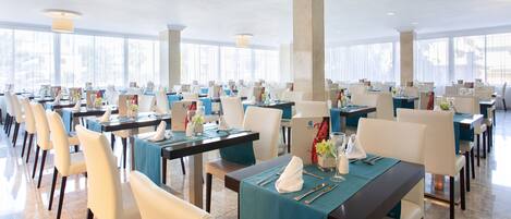 A spacious dining area with multiple tables, each set with white chairs and blue tablecloths.