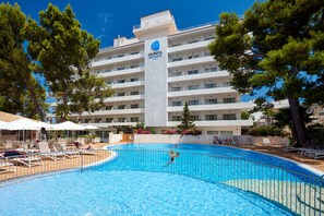 Un hotel con piscina, tumbonas y un cielo azul despejado.