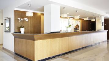 Zona de recepción con mostrador de madera, suelo de mármol e iluminación colgante.
