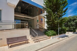 Entrada de hotel con una escalera, un banco y un letrero con el nombre del hotel.