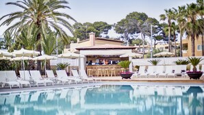 A pool area with lounge chairs and umbrellas, a bar, and palm trees.