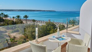 A balcony with a view of the sea, a table with a bottle and glass, and wicker chairs.