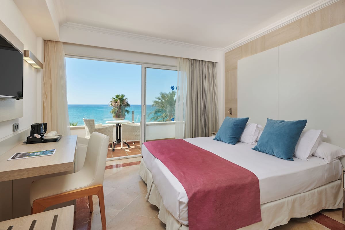 A hotel room with a bed, a desk, a chair, a TV, and a view of the ocean.