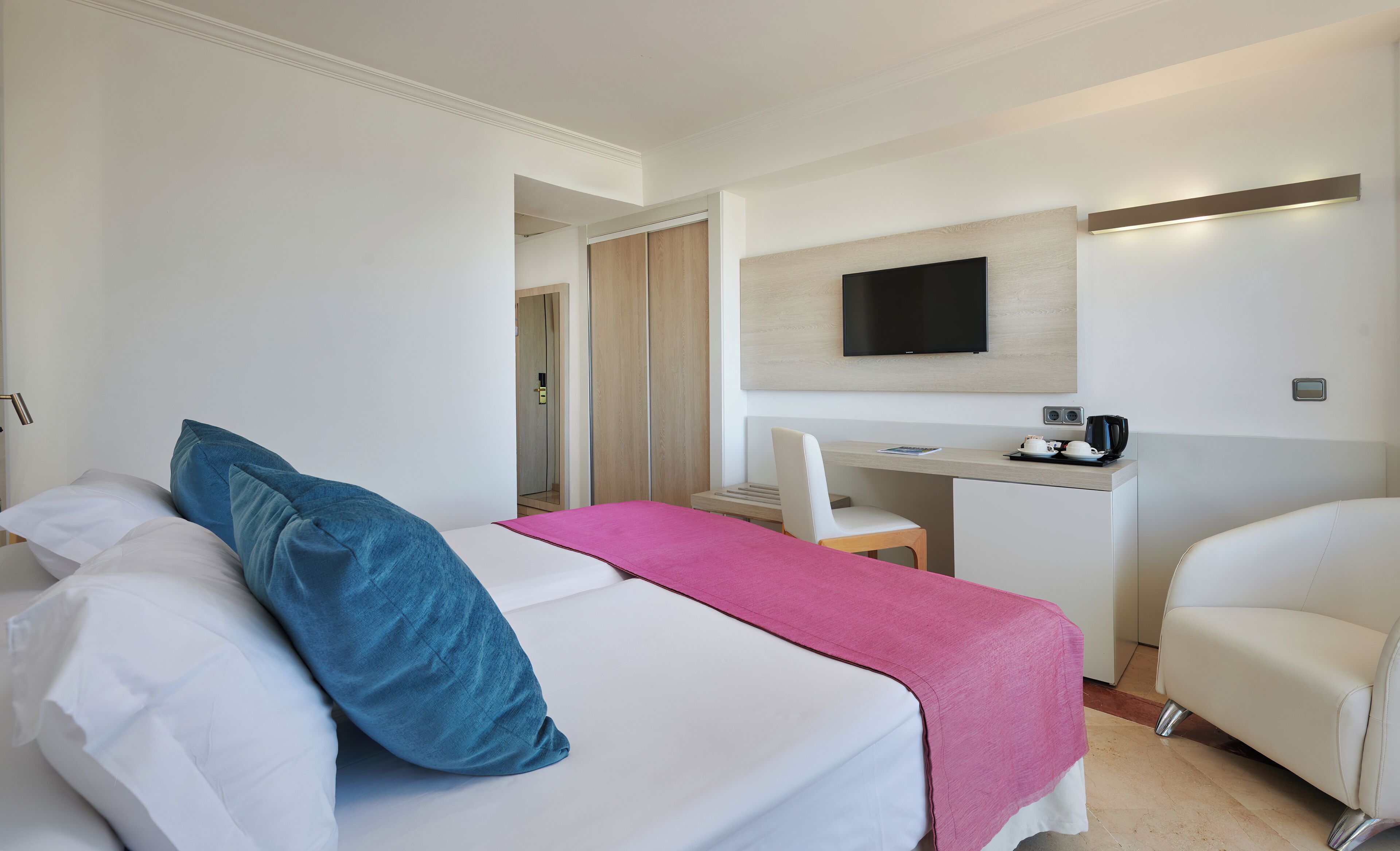 A hotel room with a bed, a desk, a chair, a TV, and a coffee maker.