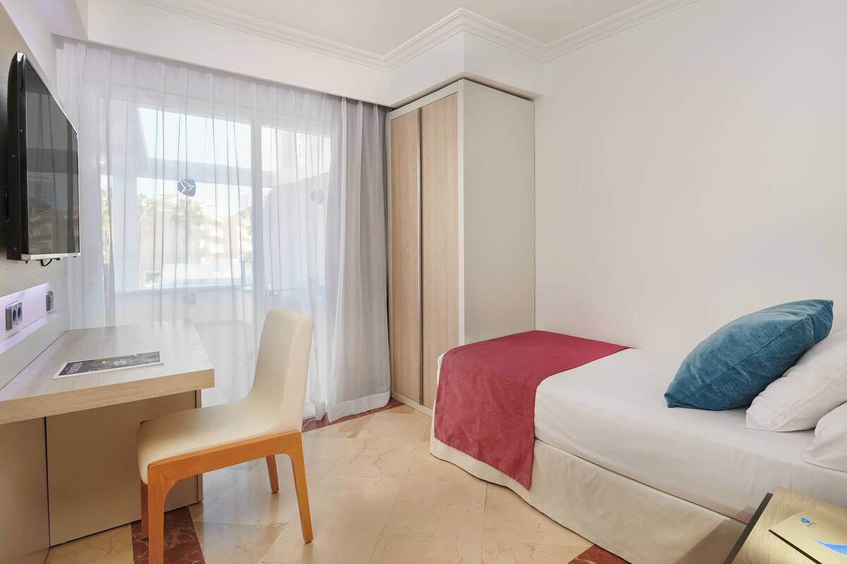 A hotel room with a bed, a desk, a chair, a TV, and a window with curtains.
