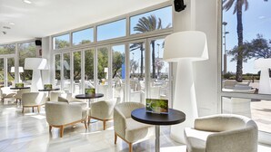 A spacious indoor area with large windows, modern chairs, and tables, featuring a view of palm trees and outdoor seating.