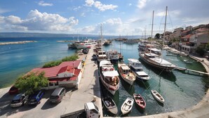 A marina with various boats docked, a parking area with cars, and buildings along the waterfront. - Hotel Krilo (Dugi Rat)