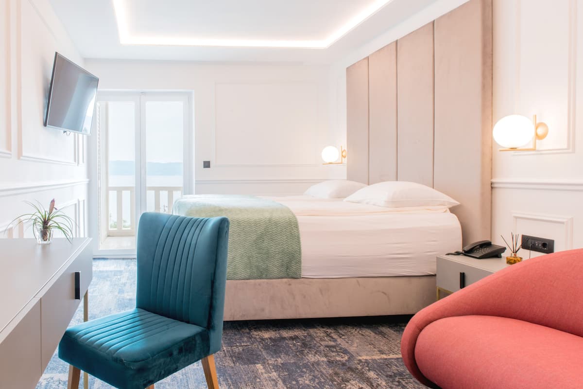 Quarto de hotel com cama, escrivaninha, cadeira e televisão na parede.