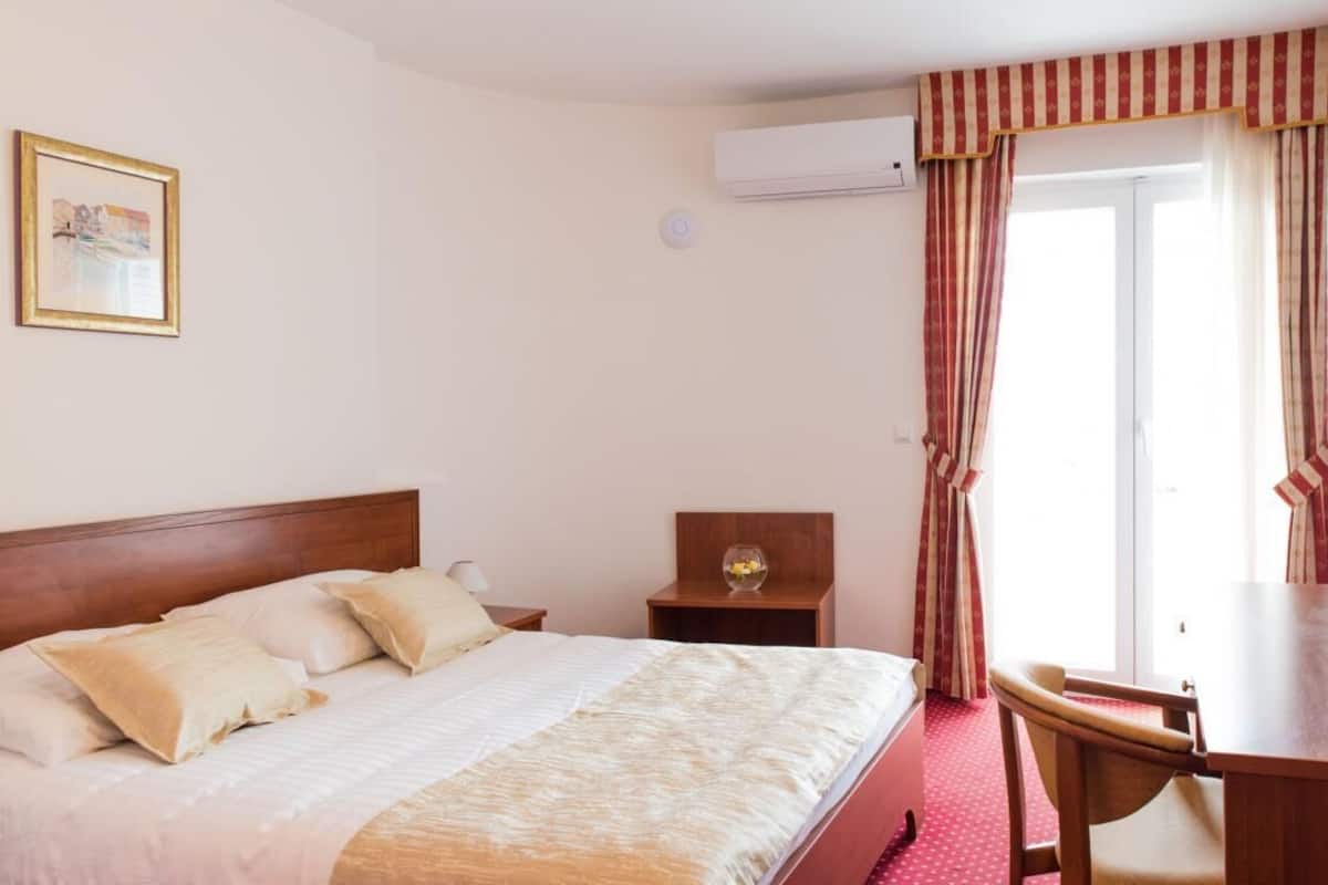 Quarto de hotel com cama, mesa de cabeceira, abajur e uma mesinha com objeto decorativo.