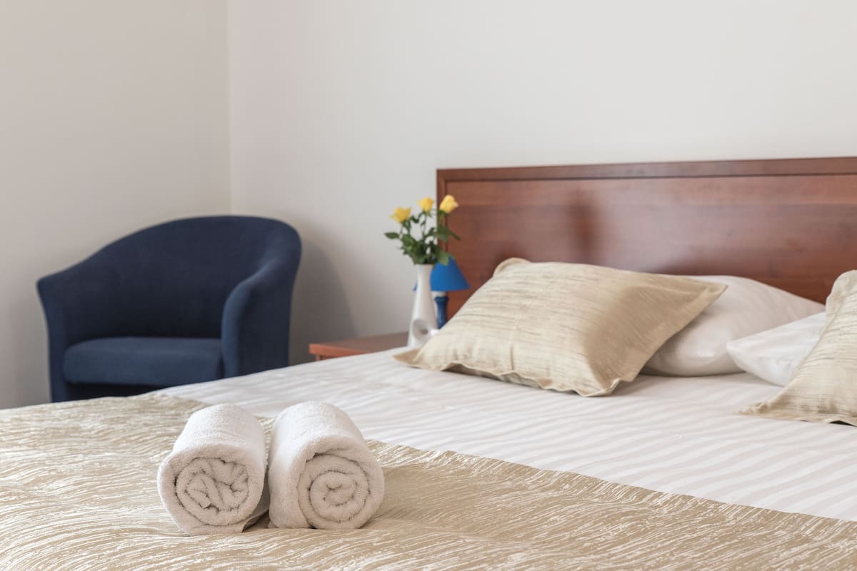 Uma cama bem arrumada com toalhas dobradas, uma cabeceira de madeira e um vaso com flores em uma mesinha de cabeceira.