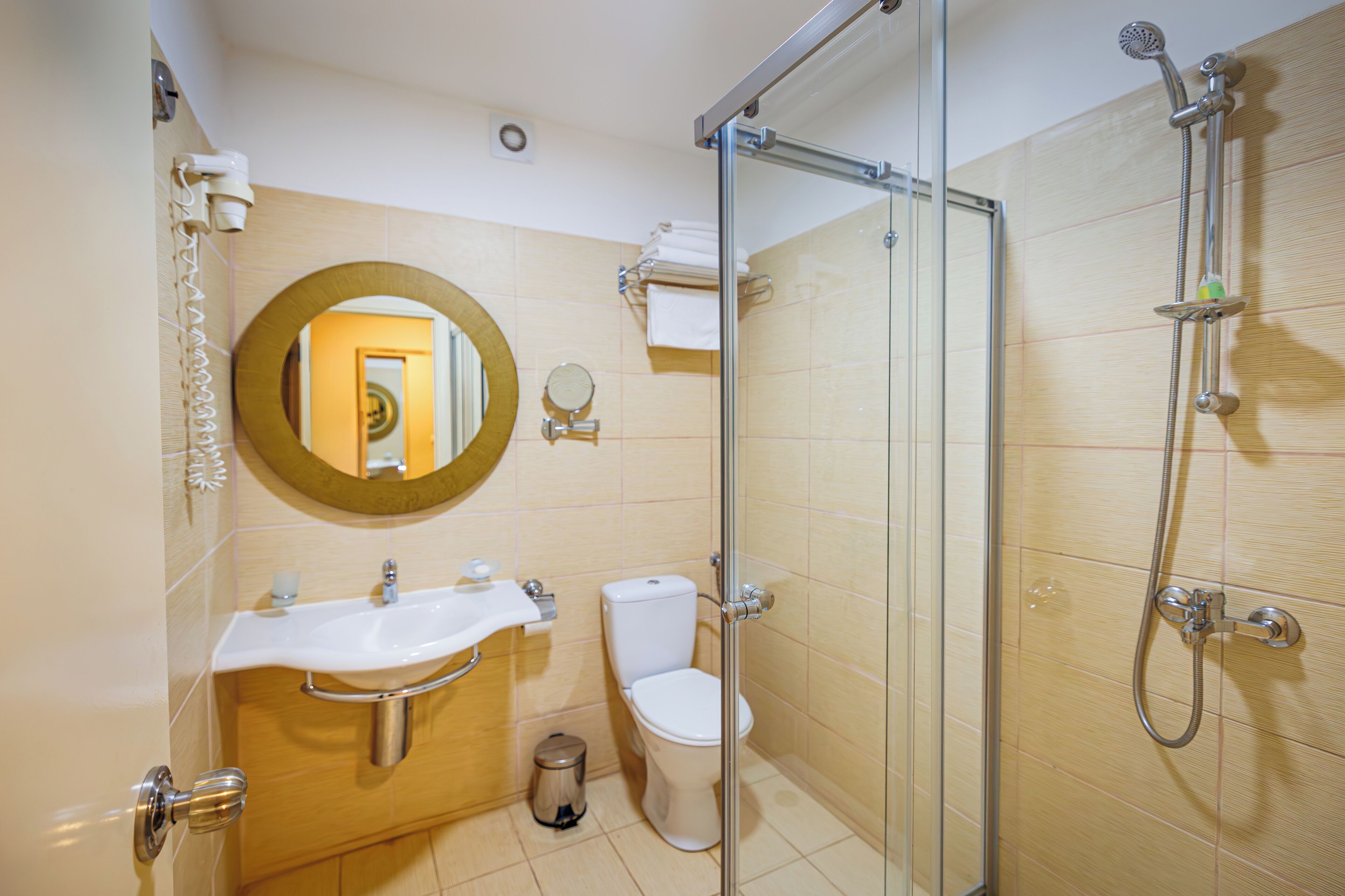 Un baño moderno con cabina de ducha de vidrio, un lavabo con tocador, un inodoro y un espejo con marco dorado.