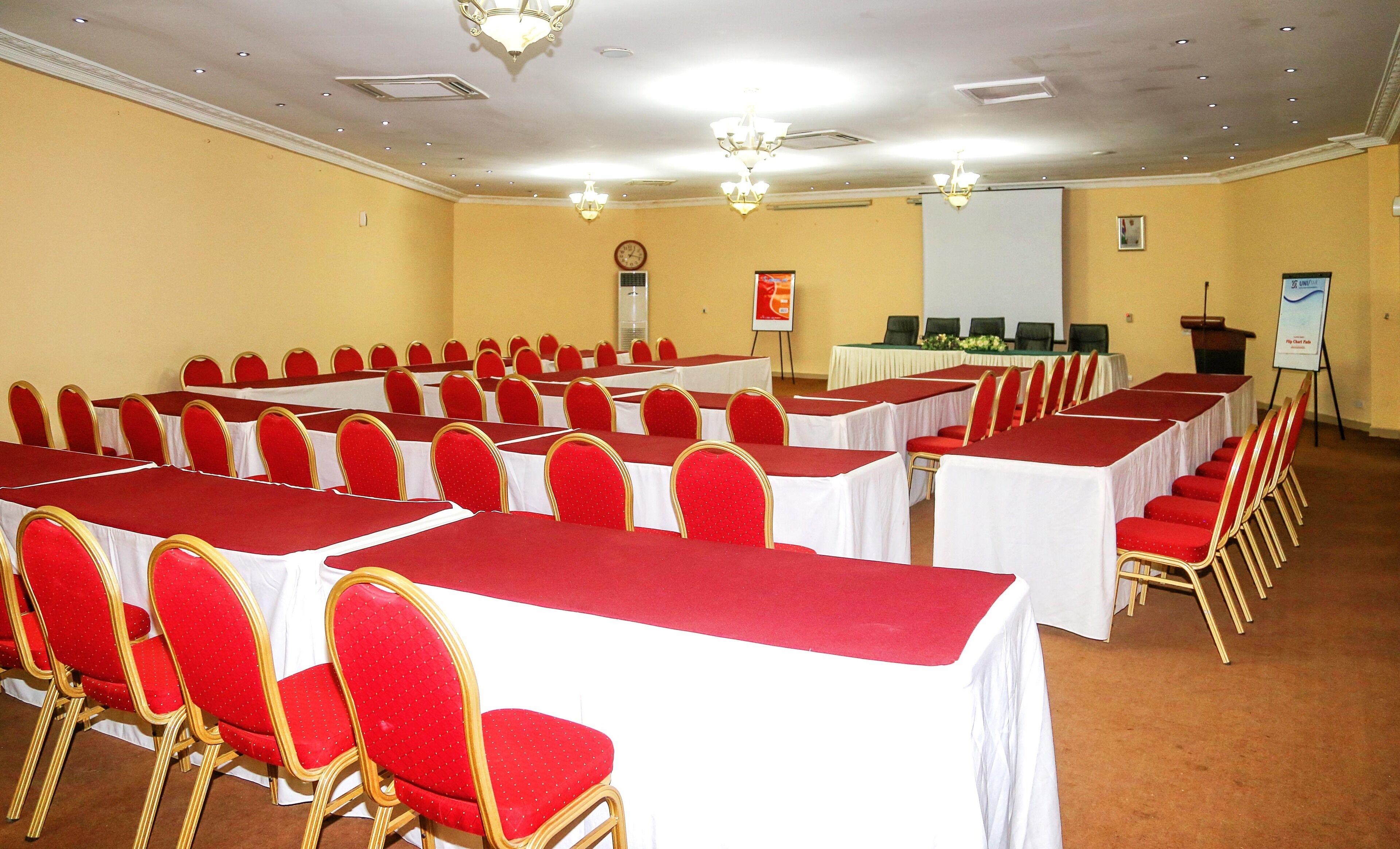 A conference room with rows of tables and chairs, a projector screen, and a podium.